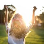 A woman with outstretched arms celebrates the sunset in a grassy field, capturing the essence of freedom and joy.